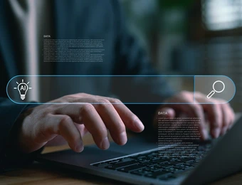 Nahaufnahme: Person tippt auf Laptop; holografische Suchleiste mit AI-Icon links, Lupe rechts.