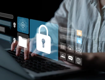 Person tippt auf Laptop; schwebende blaue Sicherheits-Icons, zentrales Vorhängeschloss.