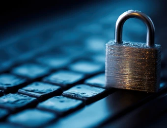 Nahaufnahme eines Metallvorhängeschlosses auf einer Tastatur, blau beleuchtet.