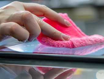 Nahaufnahme einer Hand, die einen pinken Mikrofaserlappen über eine glänzende, reflektierende Oberfläche reibt.