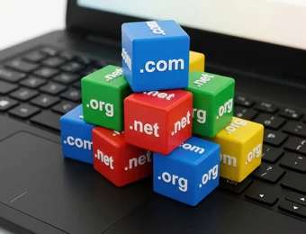 Auf einer Laptop-Tastatur stapeln sich bunte Würfel mit Domain-Endungen wie .com, .net und .org.