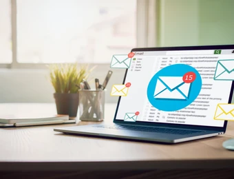 Laptop auf Schreibtisch, Bildschirm zeigt E-Mail-Symbol in Blau mit Benachrichtigungen; Pflanze, Notizbuch und Stifte daneben.