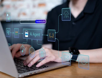 Eine Person tippt auf einem Laptop; schwebende blaue UI-Icons über der Tastatur; Armbanduhr am Arm, unscharfer Hintergrund.