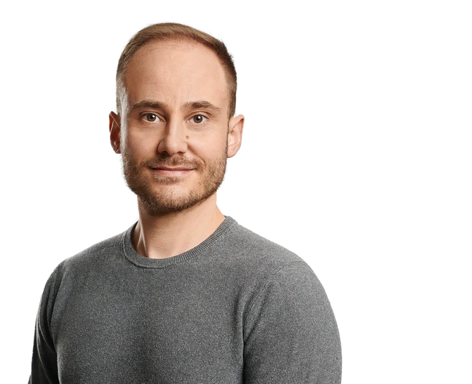 Porträt eines Mannes mit grauem Langarmshirt, blickt in die Kamera, Hintergrund mit farbigen Streifen.