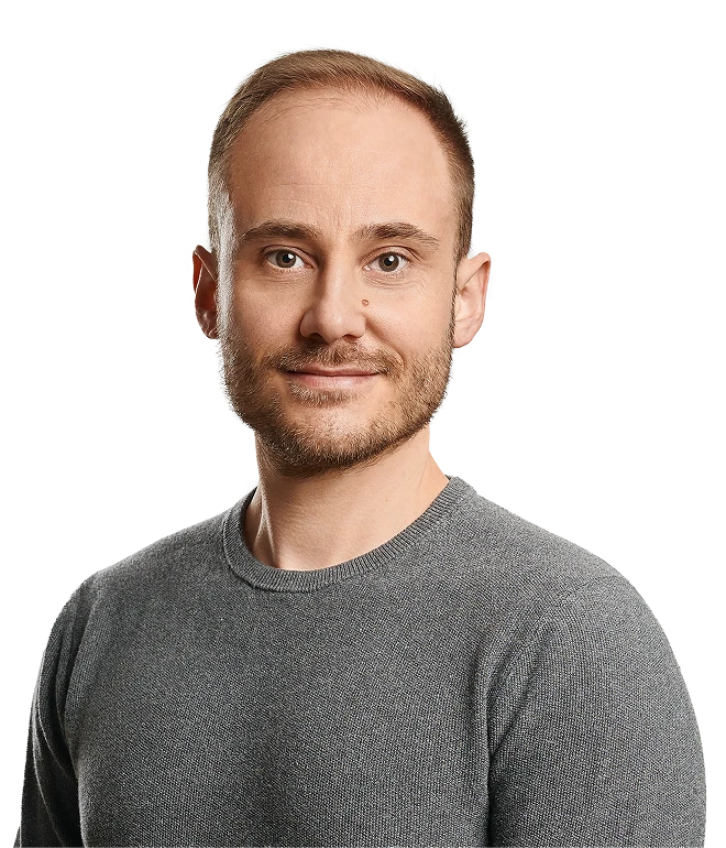 Porträt eines Mannes in grauem Pullover, kurze hellbraune Haare, leichter Bart, frontaler Blick.