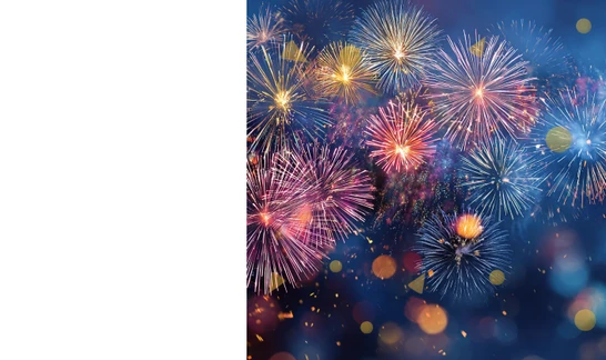 Nächtliche Szene mit bunten Feuerwerk-Explosionen in Rot, Blau und Gelb sowie Lichtern im Hintergrund.