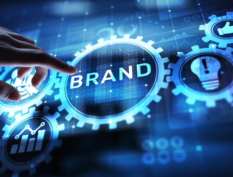 Eine Hand über einer leuchtenden Zahnradscheibe mit dem Wort BRAND, umgeben von weiteren Zahnrädern und digitalen Symbolen.