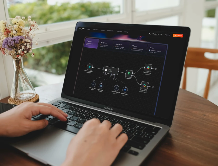 Person tippt auf Laptop; Bildschirm zeigt Diagramm/Flowchart. Vase mit Blumen links vom Laptop; Fenster im Hintergrund.