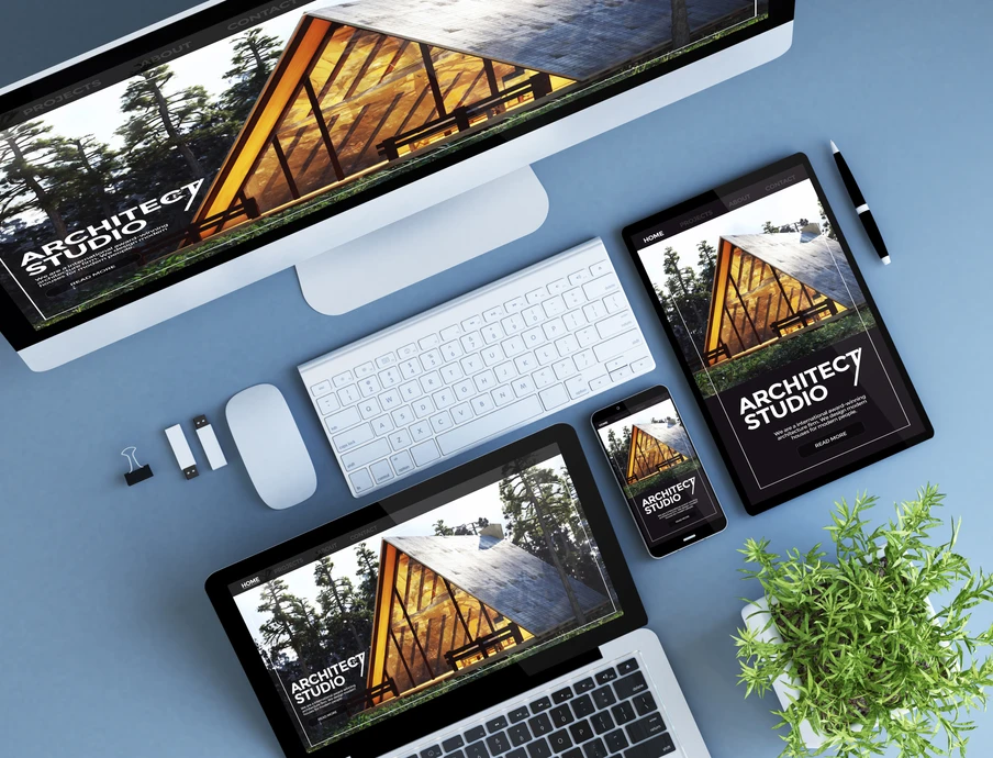 Monitor, Tablet, Smartphone und Laptop auf blauem Tisch; Bildschirme zeigen Architekturbild; Pflanze rechts.