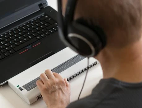 Person mit Kopfhörern vor Laptop, bedient einen weißen Controller mit vielen kleinen Tasten.