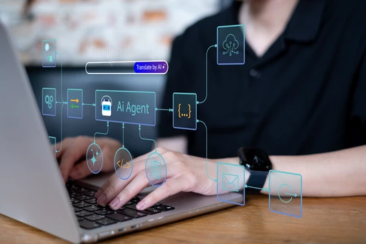 Eine Person tippt auf einem Laptop; schwebende blaue UI-Icons über der Tastatur; Armbanduhr am Arm, unscharfer Hintergrund.