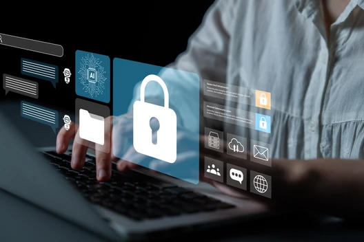 Person tippt auf Laptop; schwebende blaue Sicherheits-Icons, zentrales Vorhängeschloss.