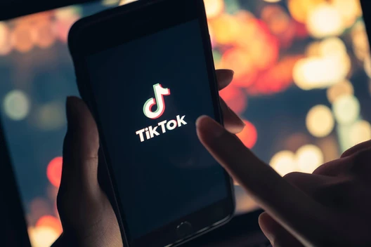 Nahaufnahme eines Smartphones mit dem TikTok-Logo auf dem Bildschirm; unscharfer, bunter Hintergrund.