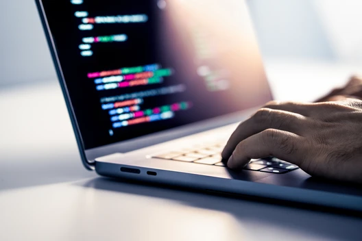 Nahaufnahme eines Laptops mit farbigem Code im Display; eine Hand tippt auf der Tastatur.